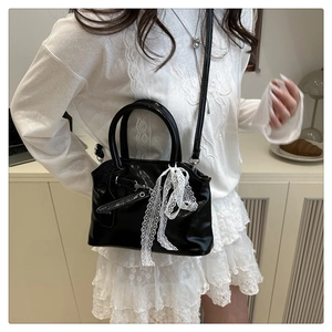 Détail du sac coquille noir brillant avec nœud en dentelle blanche porté par le modèle