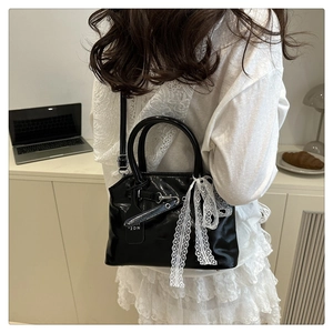 Détail d'un sac coquille noir brillant orné d'un nœud en dentelle blanche et bandoulière