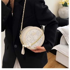 Detailed embroidery on a round crossbody bag with gold chain and pearl accents