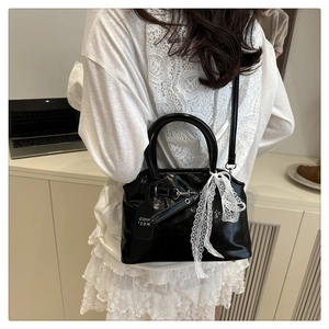 Détail du sac coquille noir brillant avec ruban en dentelle et boucles métalliques