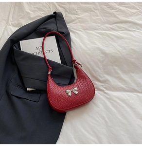 Detail of red croc-embossed hobo bag featuring a silver bow buckle and knotted handle