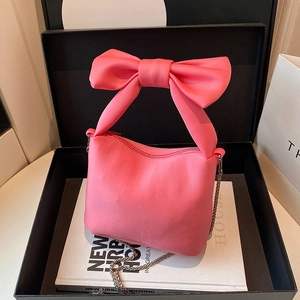 Pink satin bow handbag with metallic chain strap shown in an elegant gift setting