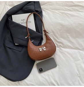Brown faux crocodile leather crescent bag with silver bow accent on draped white fabric