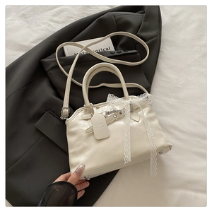 Détail d'un sac en cuir beige avec nœud en dentelle et accessoires métalliques fins