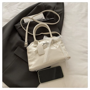 Détail du sac cabas crème avec nœud en dentelle blanche et finitions en métal argenté