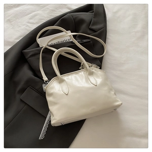 Détail du sac beige sur costume noir avec pieds en métal et bandoulière en cuir