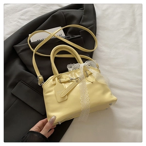 Détail du sac Boston en cuir jaune clair avec nœud en dentelle et pendentif de marque