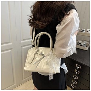 Détail du sac coquille en cuir verni blanc avec nœud en dentelle et bandoulière