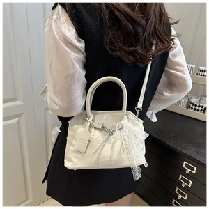 Vue détaillée du sac coquille blanc avec nœud en dentelle et étiquette en cuir sur le côté