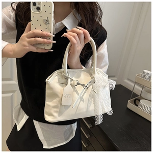 Détail du sac coquillage crème avec finition brillante et nœud en dentelle blanche