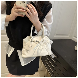 Détail du sac à main en cuir verni crème avec nœud en dentelle et pendentif élégant