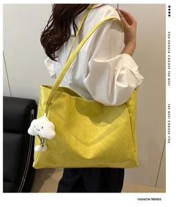 Vista dettagliata della borsa tote gialla in finto camoscio con ciondolo a nuvola sulla spalla