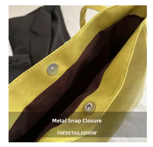Detail view of silver magnetic buckle on yellow pebbled leather tote with brown lining