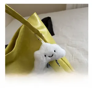 Detail of a white plush cloud charm with a smiley face on a yellow tote bag handle