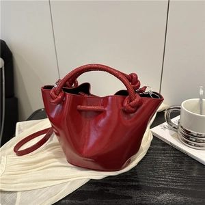 Glossy red bucket bag with pleated design and top handle on white fabric setting
