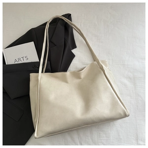 Dettaglio di una borsa tote crema minimalista con trama in pelle liscia e doppi manici