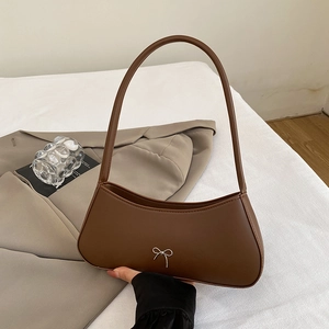 Brown faux leather crescent shoulder bag with silver bow accent on warm fabric background