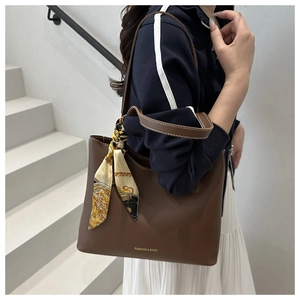 Détail du sac cabas en cuir marron avec logo doré et foulard en soie jaune décoratif