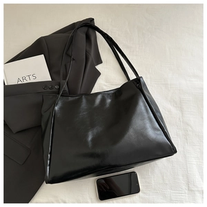 Piatto di una grande borsa tote nera lucida con accessori da ufficio su fondo bianco