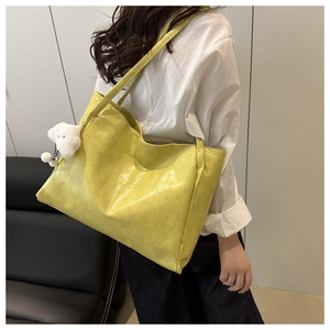 Close-up of a large yellow leather tote bag featuring a white plush cloud charm accessory