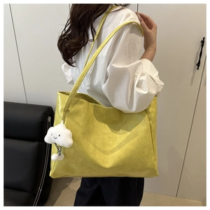 Detailed side view of a large yellow leather tote bag with a white cloud charm on a model