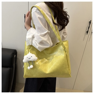 Vista laterale di una borsa tote gialla con ciondolo a nuvola bianca sulla spalla del modello