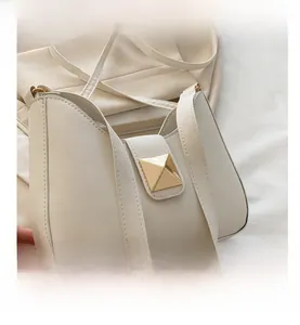 Detail view of cream white faux leather crescent bag with gold pyramid metal buckle
