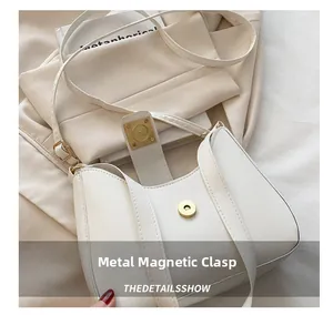 Detail shot of the white curved shoulder bag featuring a magnetic metal snap closure