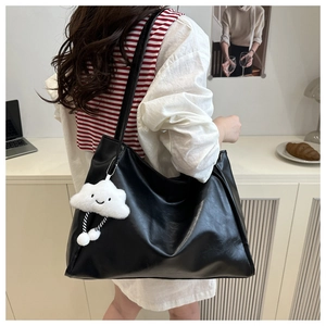 Dettaglio della grande borsa tote in pelle nera con ciondolo a nuvola bianca sulla spalla