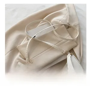 Close-up of a cream crossbody bag with a gold pyramid lock and a slim adjustable strap