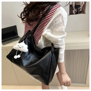 Dettaglio della borsa tote nera in ecopelle con ciondolo a nuvola sulla spalla della modella