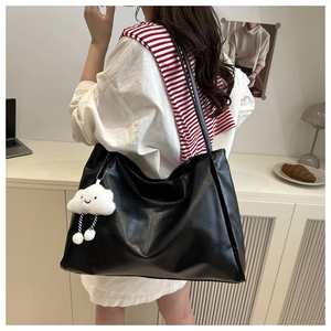 Close-up of a large black leather tote bag featuring a cute white cloud plush charm detail