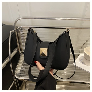Detail of black crescent shoulder bag with golden pyramid hardware on minimalist chair