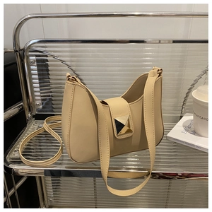 Detail of a beige crescent underarm bag featuring a golden triangular metal buckle closure