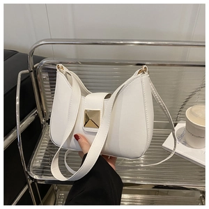 White crescent underarm bag with gold metal clasp shown in a lifestyle city setting