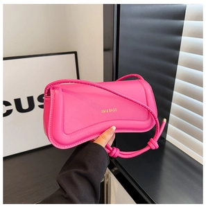 Detail of rose pink handbag featuring asymmetrical flap design and knotted strap accents