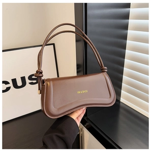 Detail of a dark brown leather underarm bag with gold logo and decorative knot strap