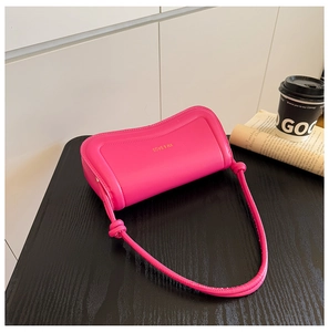 Detailed shot of pink PU leather underarm bag with gold logo and knotted strap on dark table