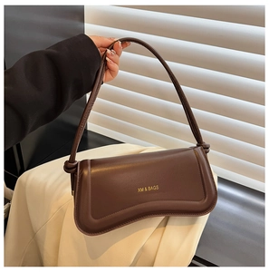 Detail of a dark brown leather underarm bag featuring a gold XM & BAGS logo and curved design