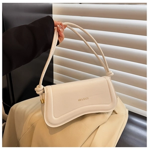 Close-up of cream leather shoulder bag featuring unique knotted handle and metal buckle