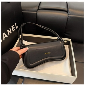 Detail of a black leather handbag with a unique rectangular shape and gold branding logo