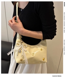 Detail of beige patent leather bag with large pearl bow and lace charm decoration