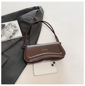 Detail of a dark brown leather bag with wavy top edge and gold logo on light background