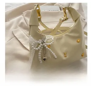 Detail of cream half-moon bag with gold bone rivets and lace pearl bow pendant