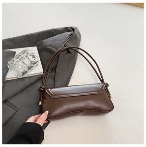 Detailed view of brown leather baguette bag with knotted strap and gold hardware
