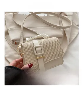 Detail shot of a beige woven crossbody bag with pearl handle and golden square buckle clasp