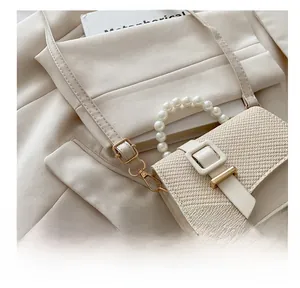 Detail of cream woven handbag featuring pearl top handle and gold adjustable buckle