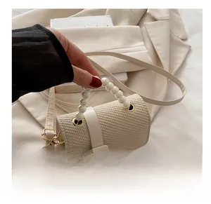 Detail of beige woven crossbody bag featuring a luxury faux pearl top handle and square clasp