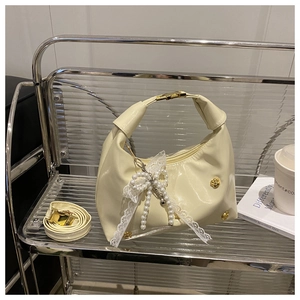 Dettaglio borsa beige lucida con ciondolo a fiocco di pizzo e perle e fibbia dorata