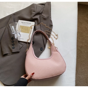 Détail du sac hobo rose tressé avec chaîne dorée dans un décor de style de vie épuré